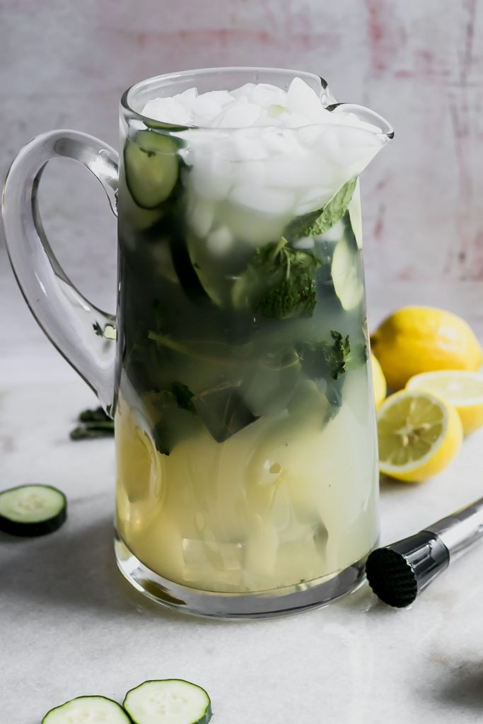 a pitcher of lemonade with cucumbers and mint on a white table