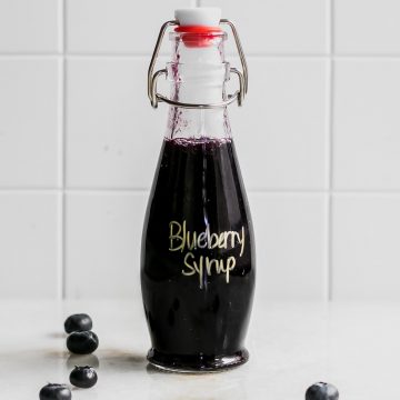 blueberry syrup on a white table with whole fresh blueberries