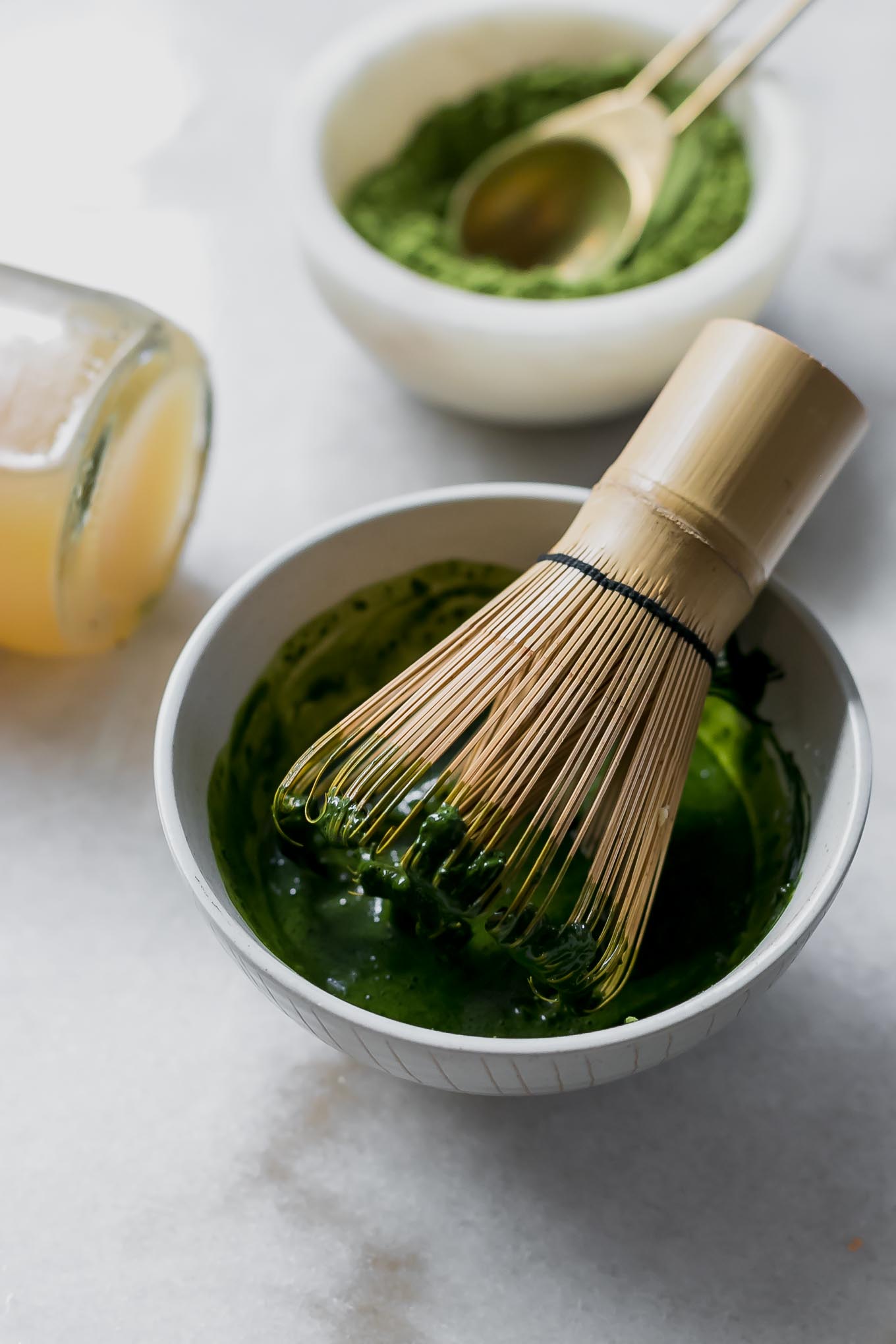 matcha in a bowl with a matcha whisk on a white countertop