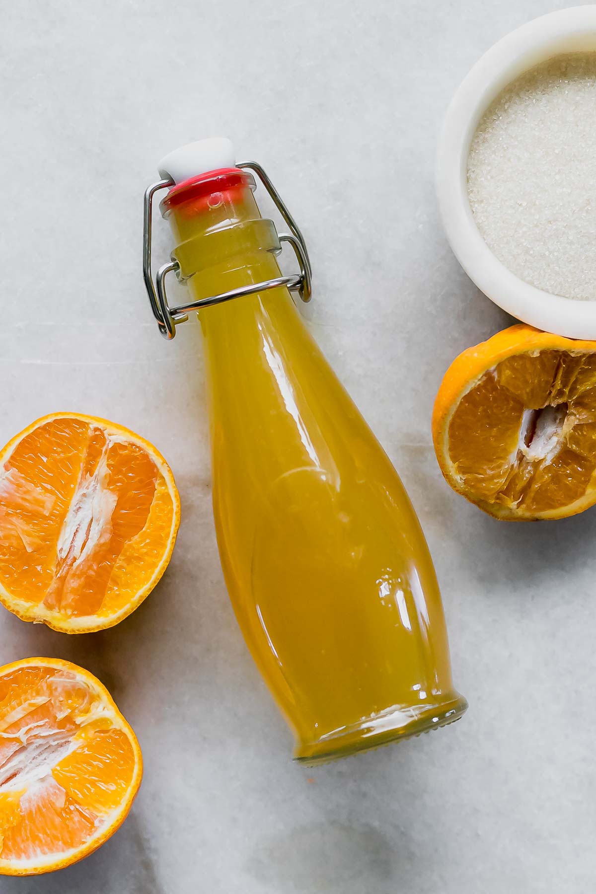 orange simple syrup in a glass jar on a table with sliced oranges