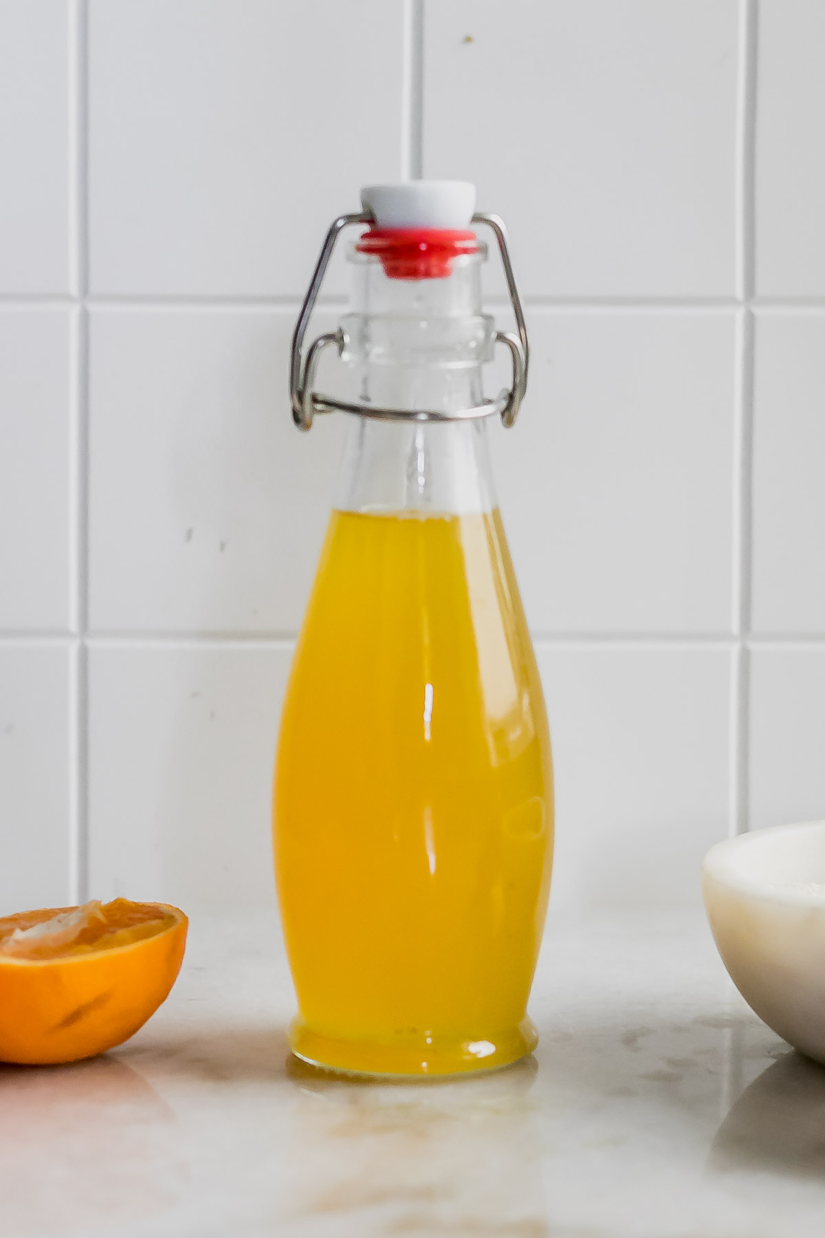 orange simple syrup in a pouring jar on a countertop