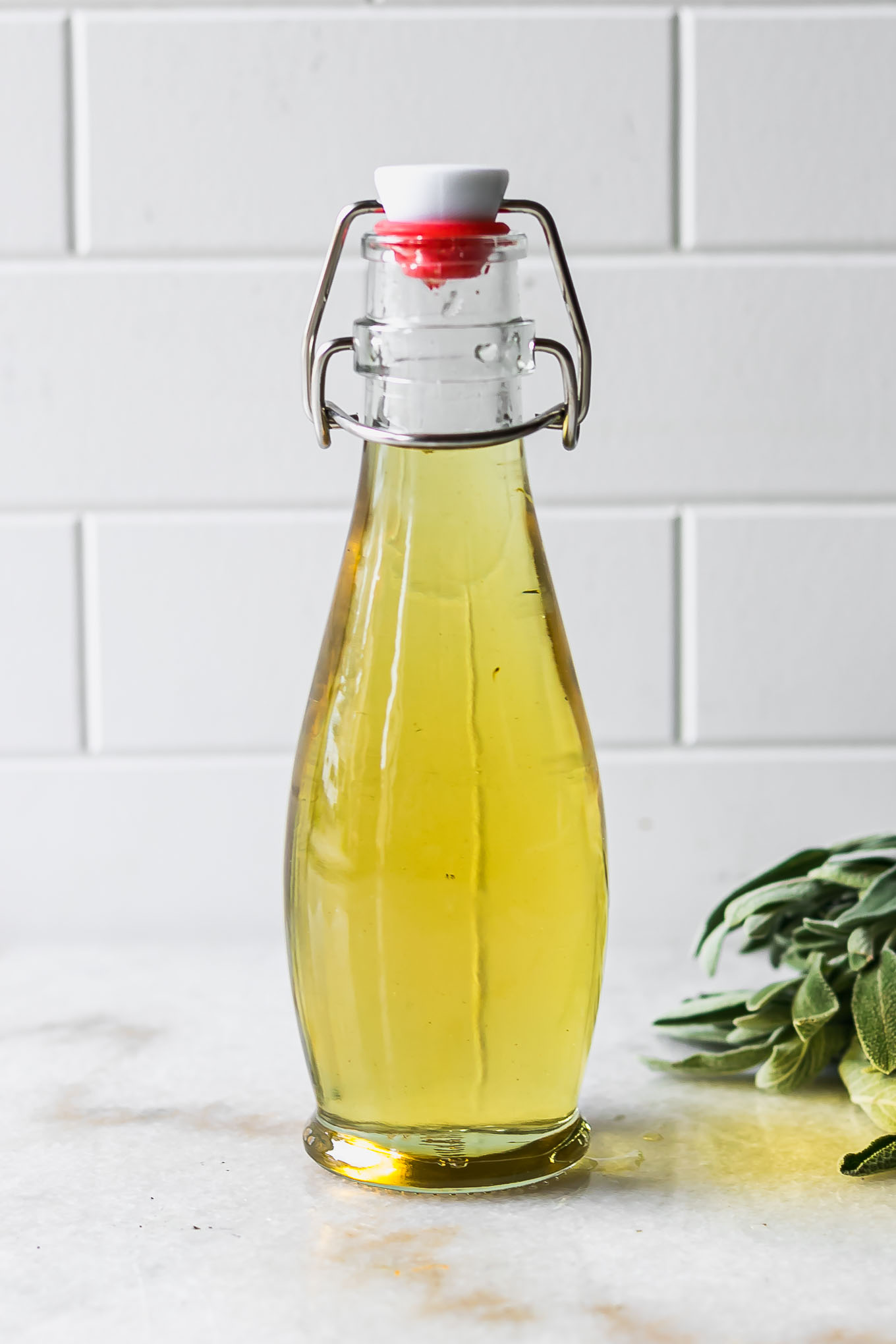 simple syrup with sage leaves in a glass bottle on a white countertop