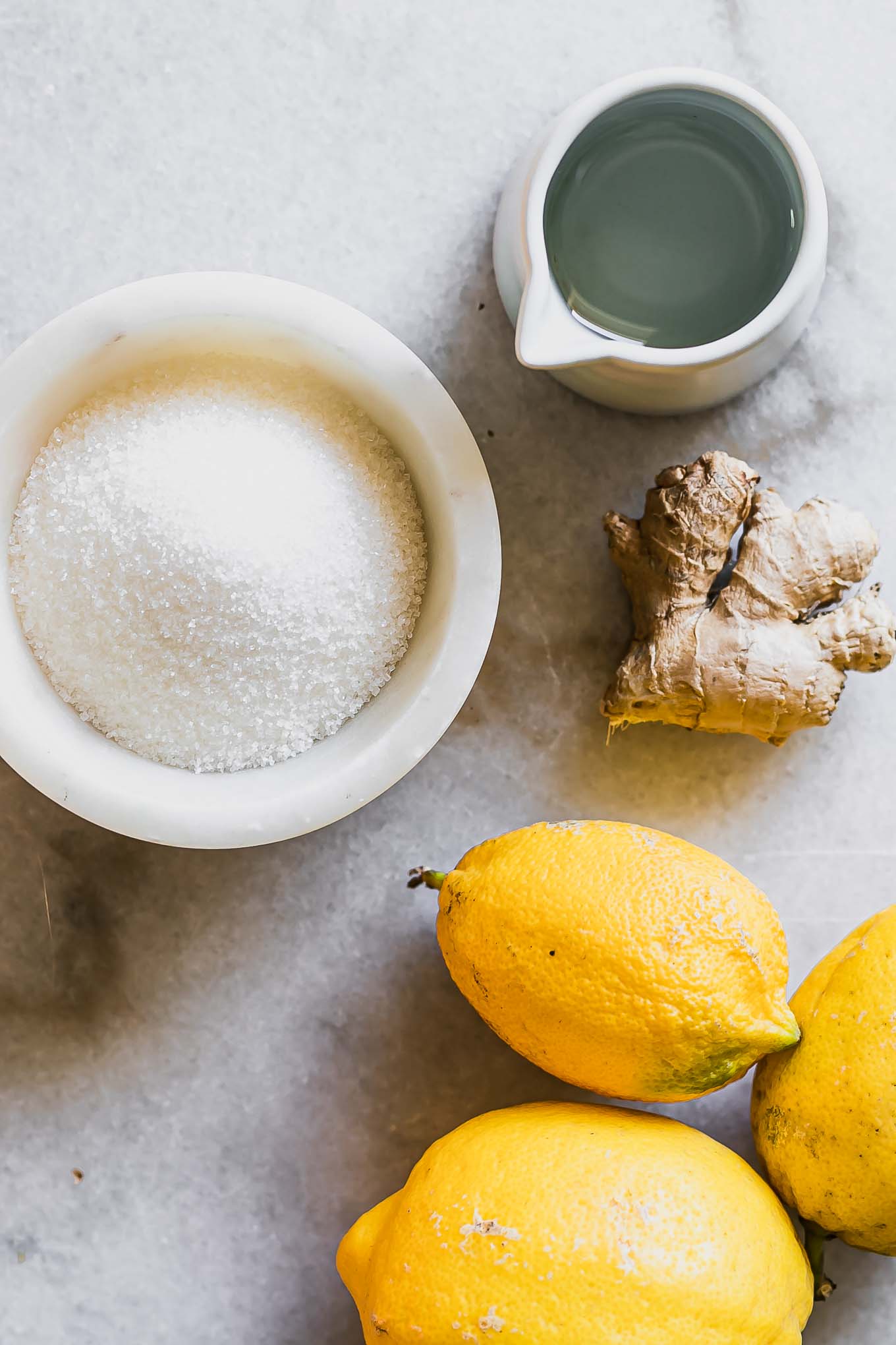 lemons, ginger, and bowls of sugar and water on a white table