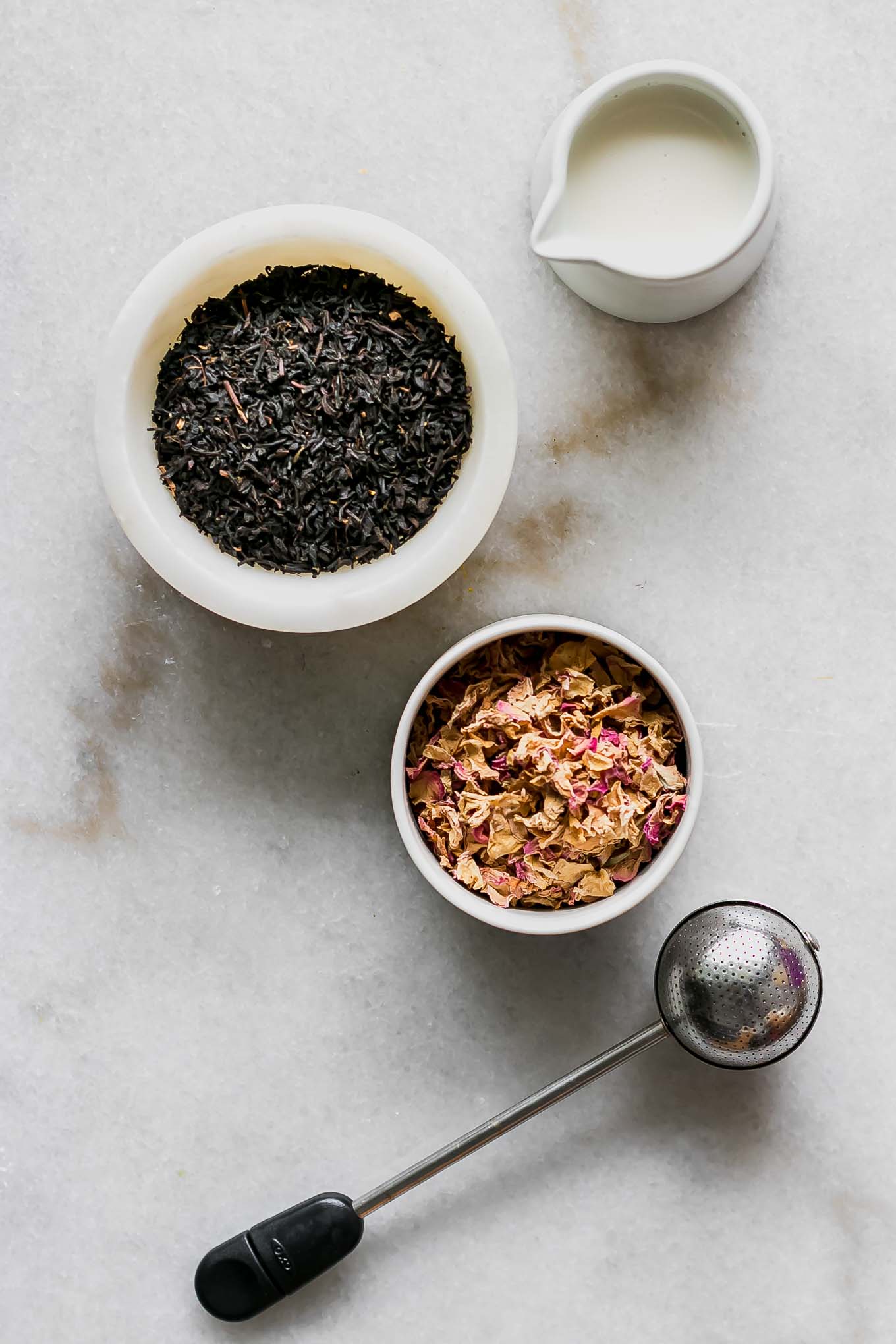 bowls of chai tea, dried rose petals, and plant-based milk on a white table