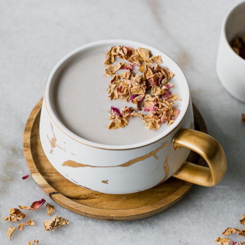 a rose chai latte in a white mug with on a marble countertop with dried rose petals