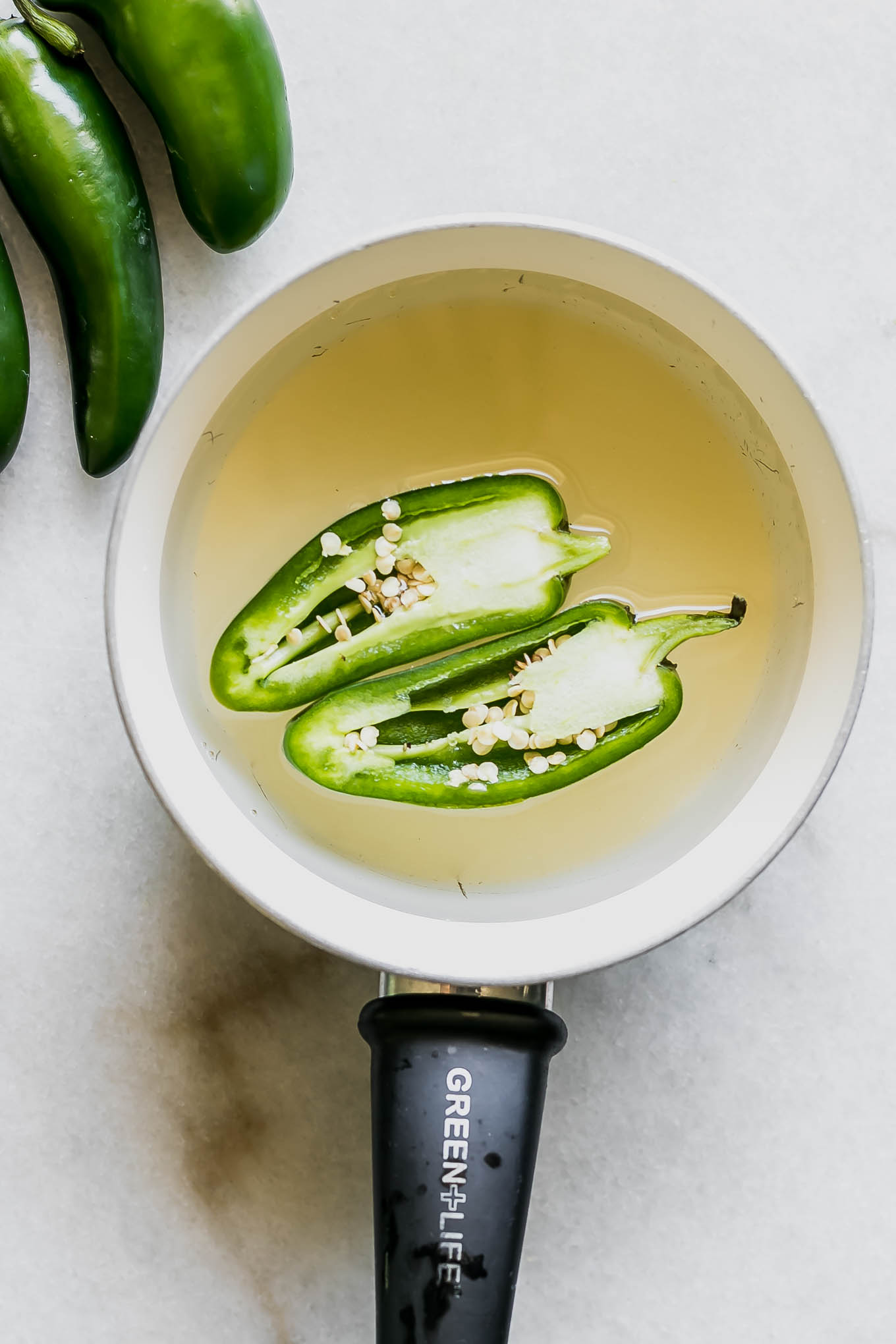 sliced jalapenos in a white saucepan with water and sugar for simple syrup