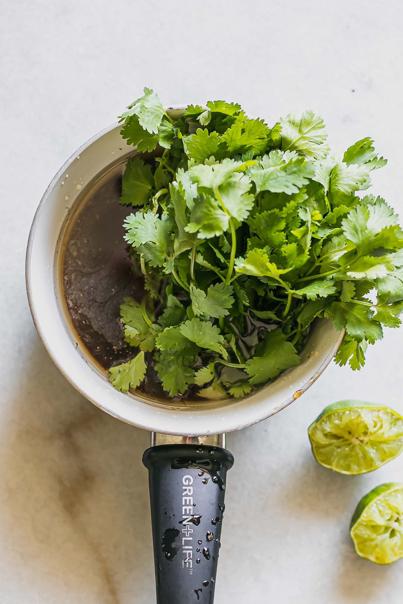 a small sauce pan with water, sugar, and cilantro on a white table
