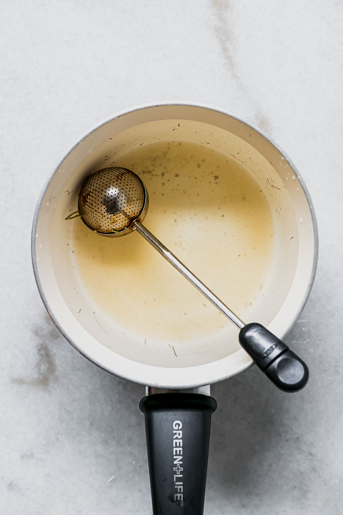 jasmine flower buds in a tea infuser in a white saucepan with water and sugar