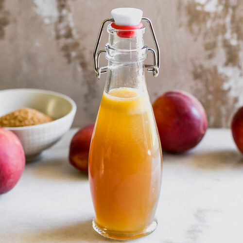 a jar of peach syrup on a counter with fresh whole peaches