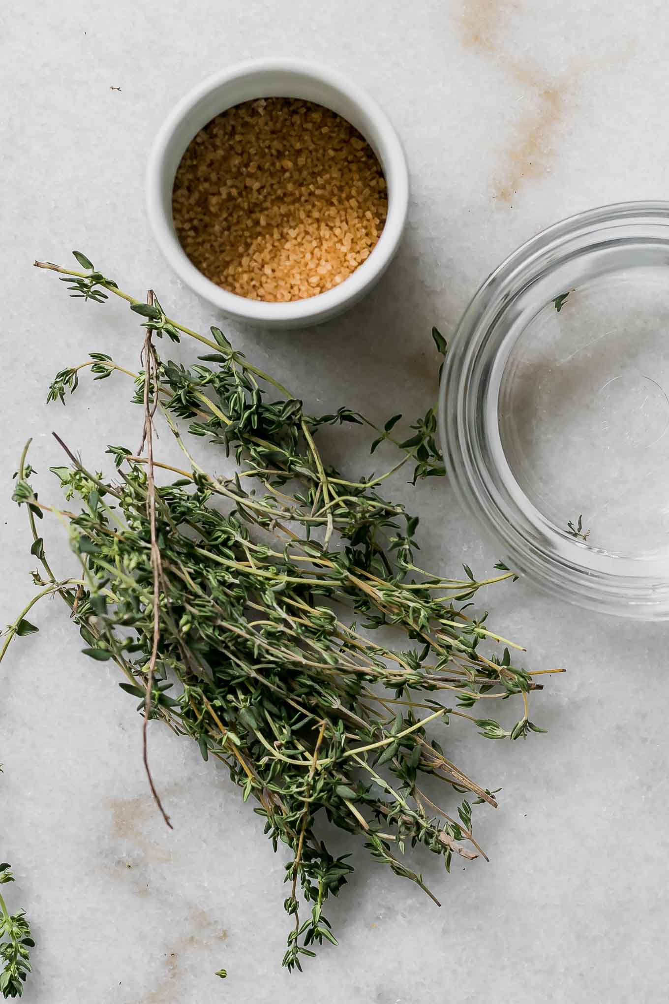 thyme sprigs, a bowl of sugar, and a cup of water on a table for simple syrup