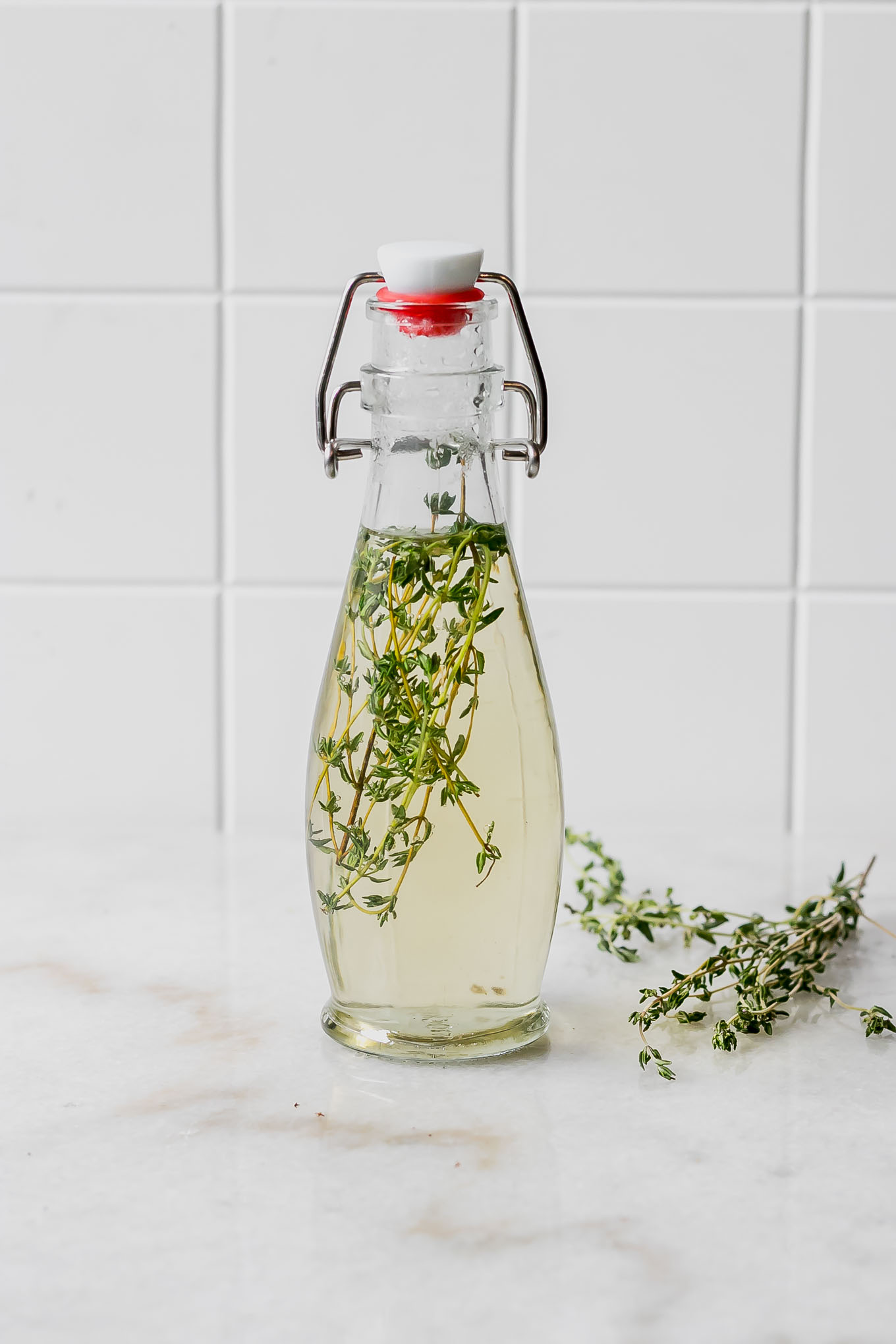 thyme sprigs in a bottle with simple syrup on a white countertop