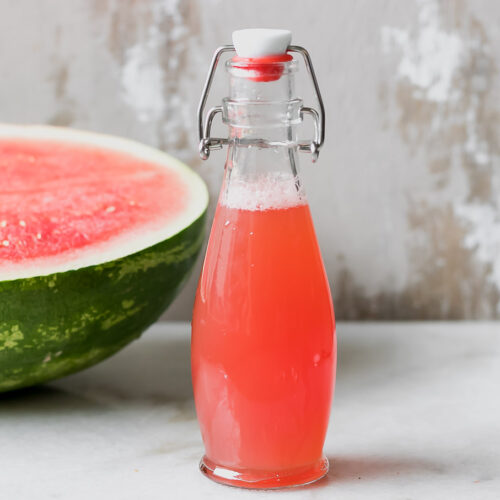 watermelon juice simple syrup in a glass jar with a half watermelon