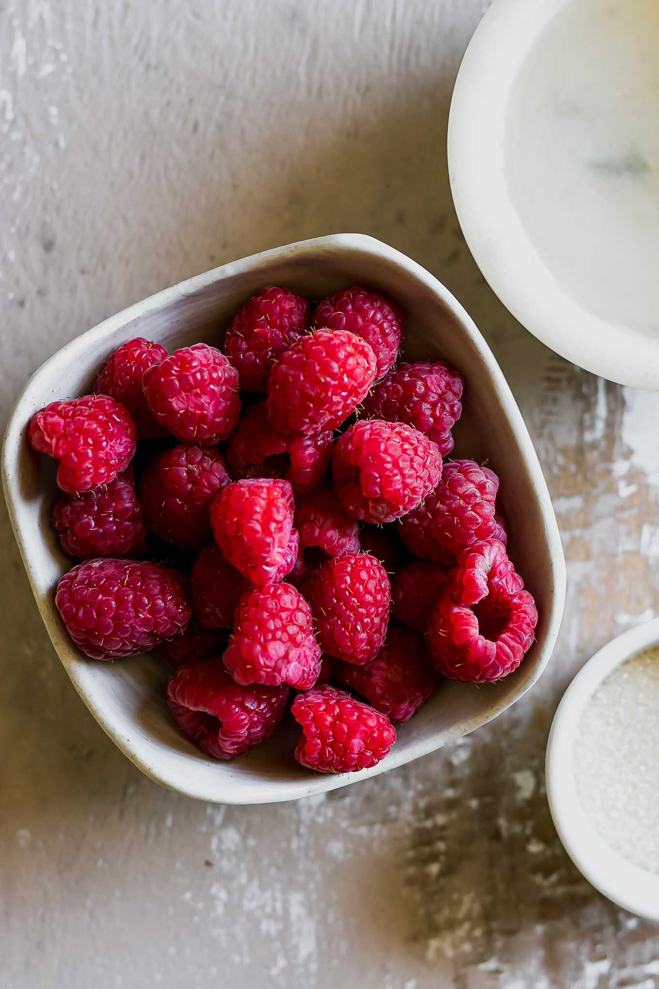 bowls of raspberries, water, and sugar on a wood table