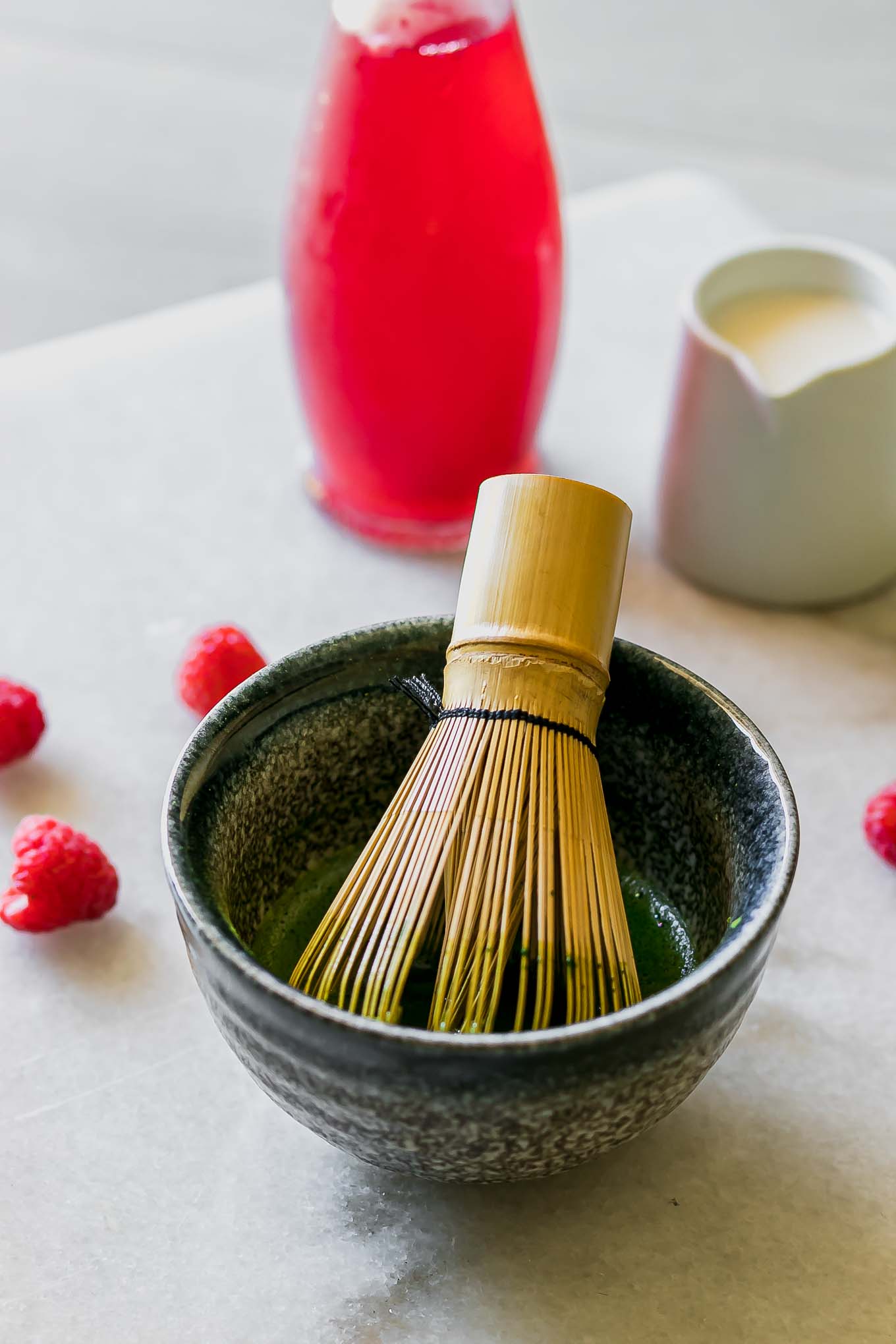 a bowl of green matcha powder and a matcha whisk on a white table