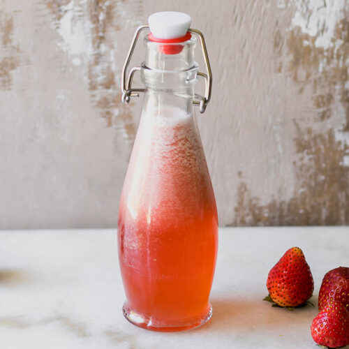 strawberry-infused syrup in a glass jar on a white countertop