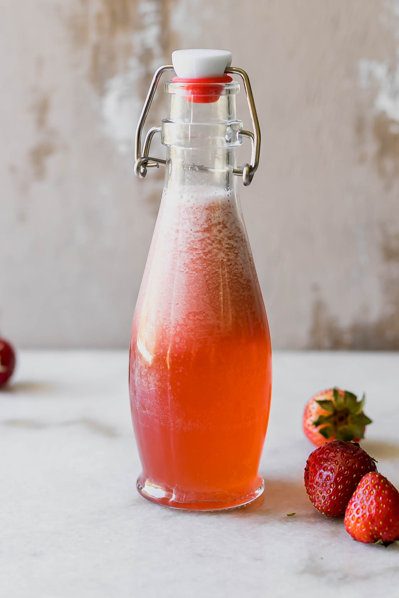 strawberry simple syrup in a glas jar on a countertop with strawberries