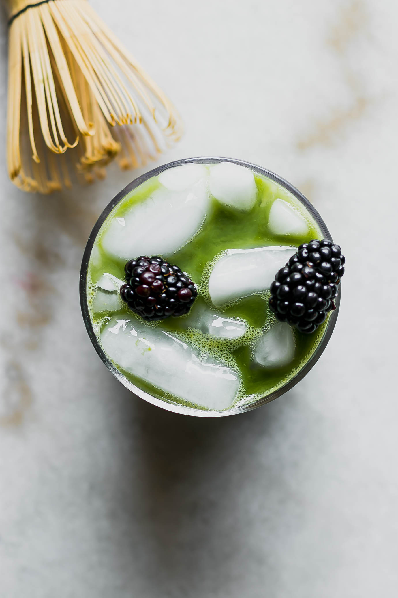 a close up photo of a green matcha iced latte with blackberry syrup and two blackberries as garnish on top