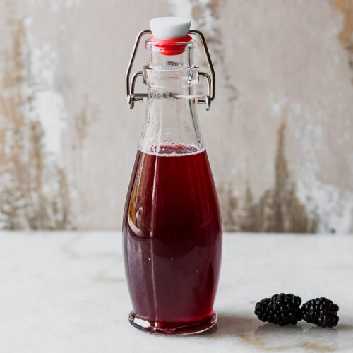 a jar of blackberry syrup on a white countertop with fresh blackberries
