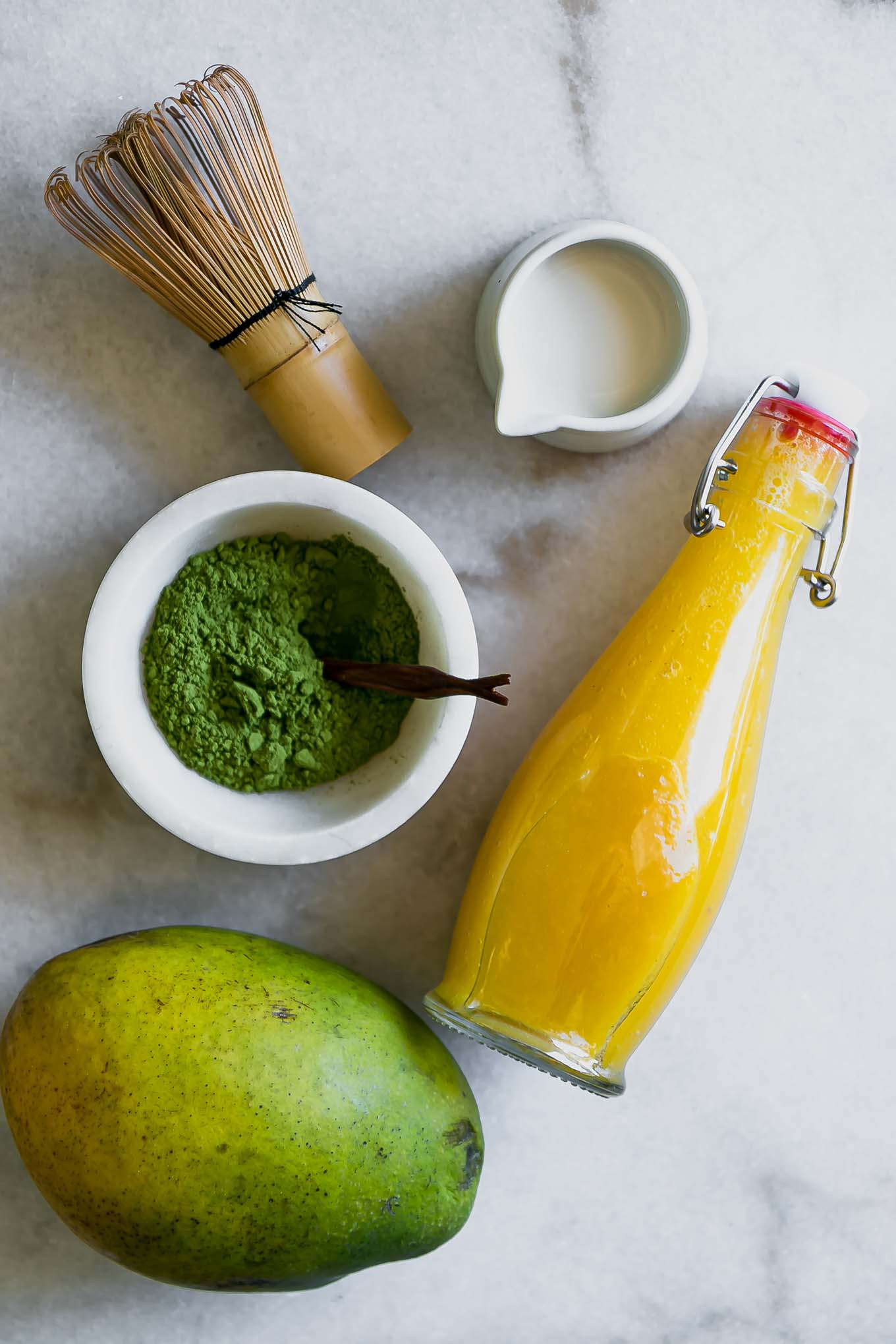 a bowl of matcha, milk, and mango syrup on a table with a match whisk