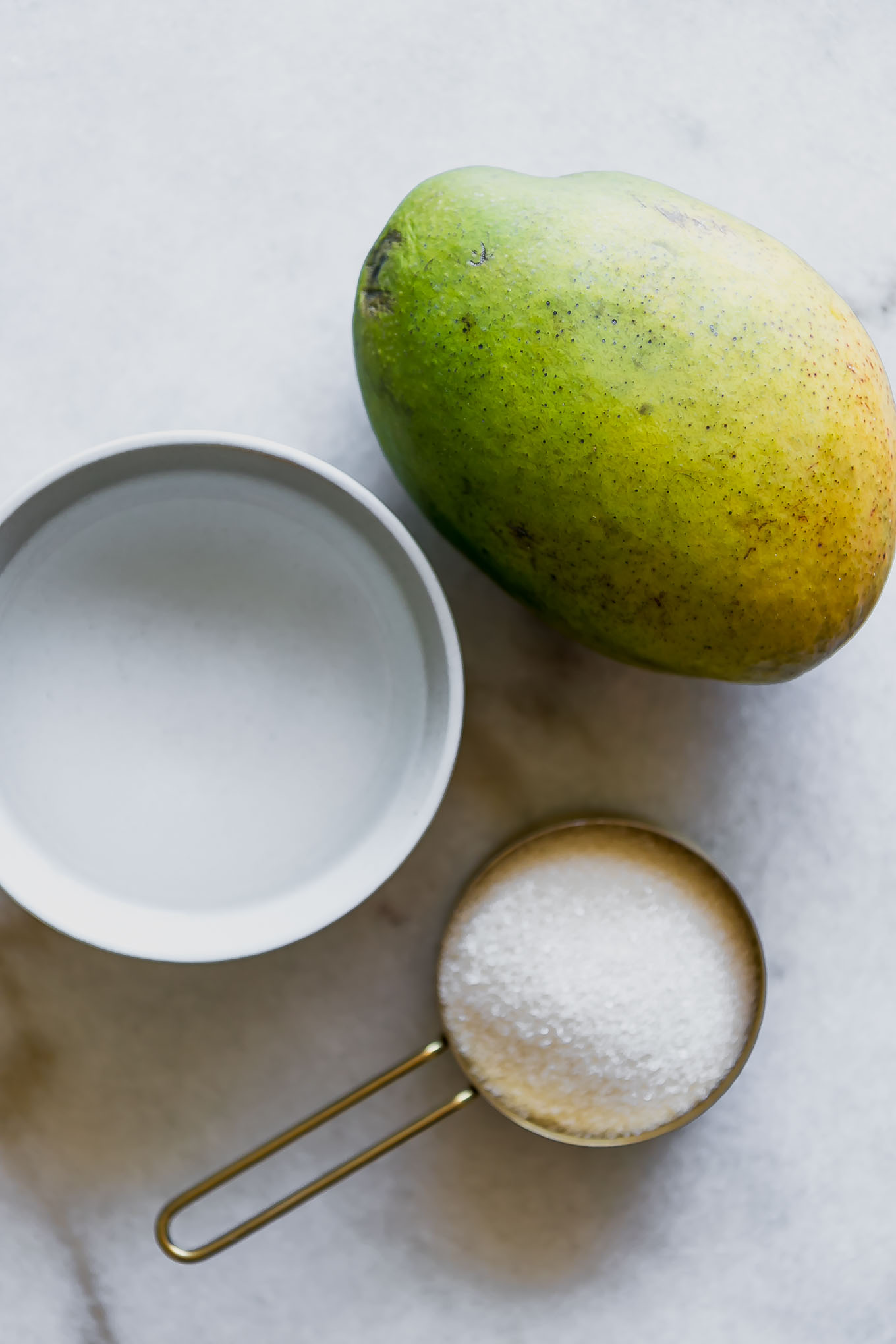 a bowl of water, sugar, and a whole mango on a white table