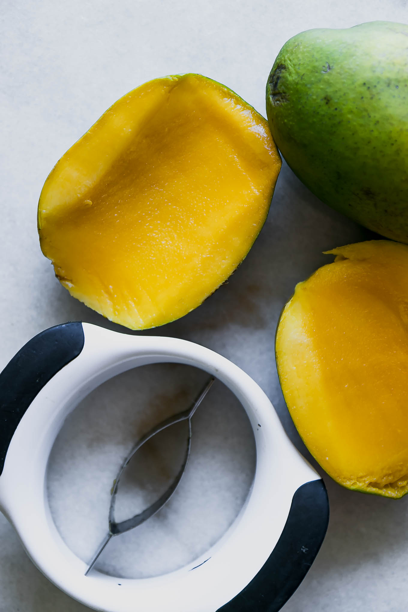 two mango halves on a white table with a mango cutter