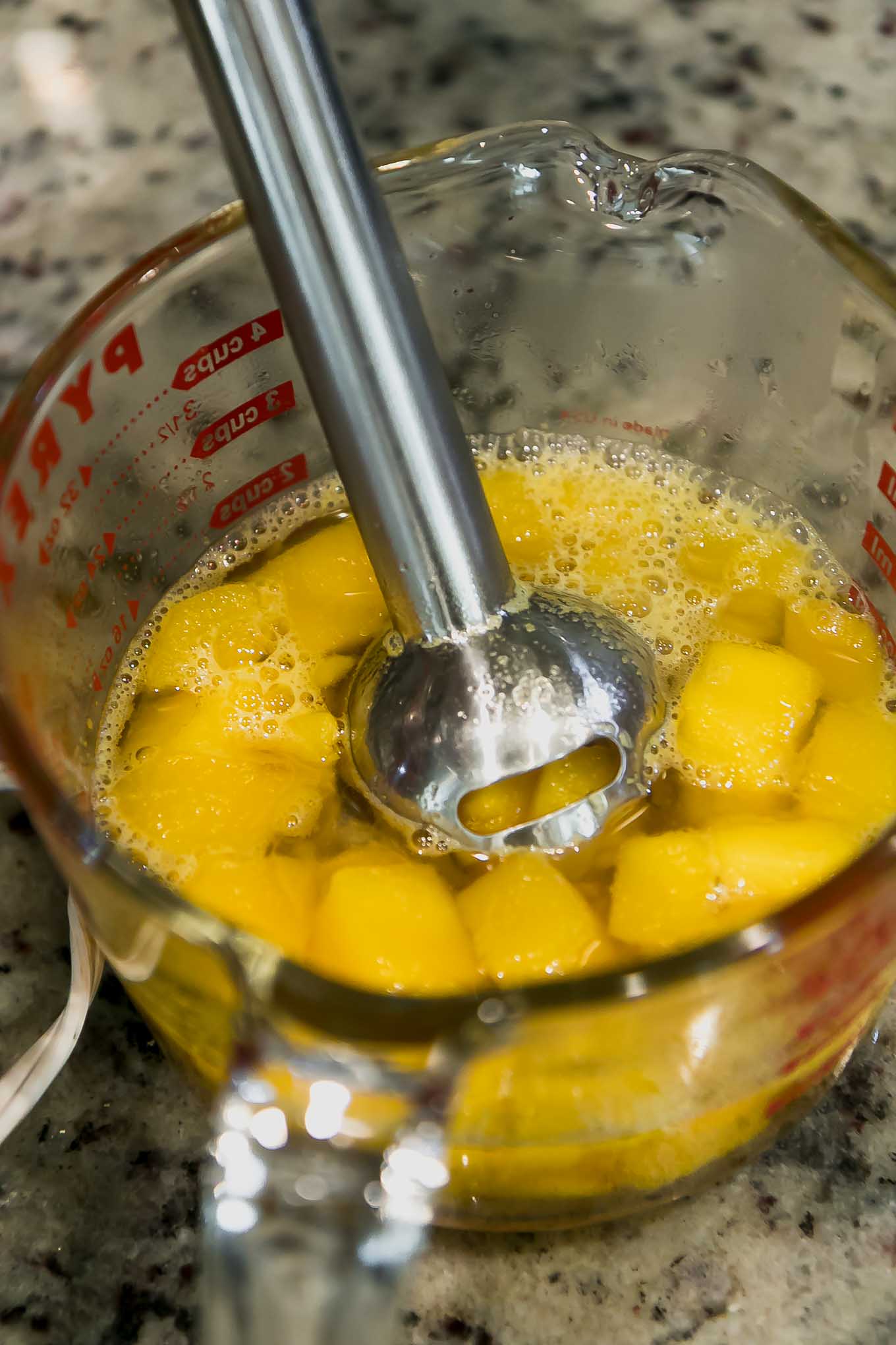 mango simple syrup in a measuring bowl with an immersion blender