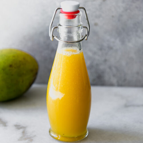 yellow mango syrup in a jar on a white table with a mango