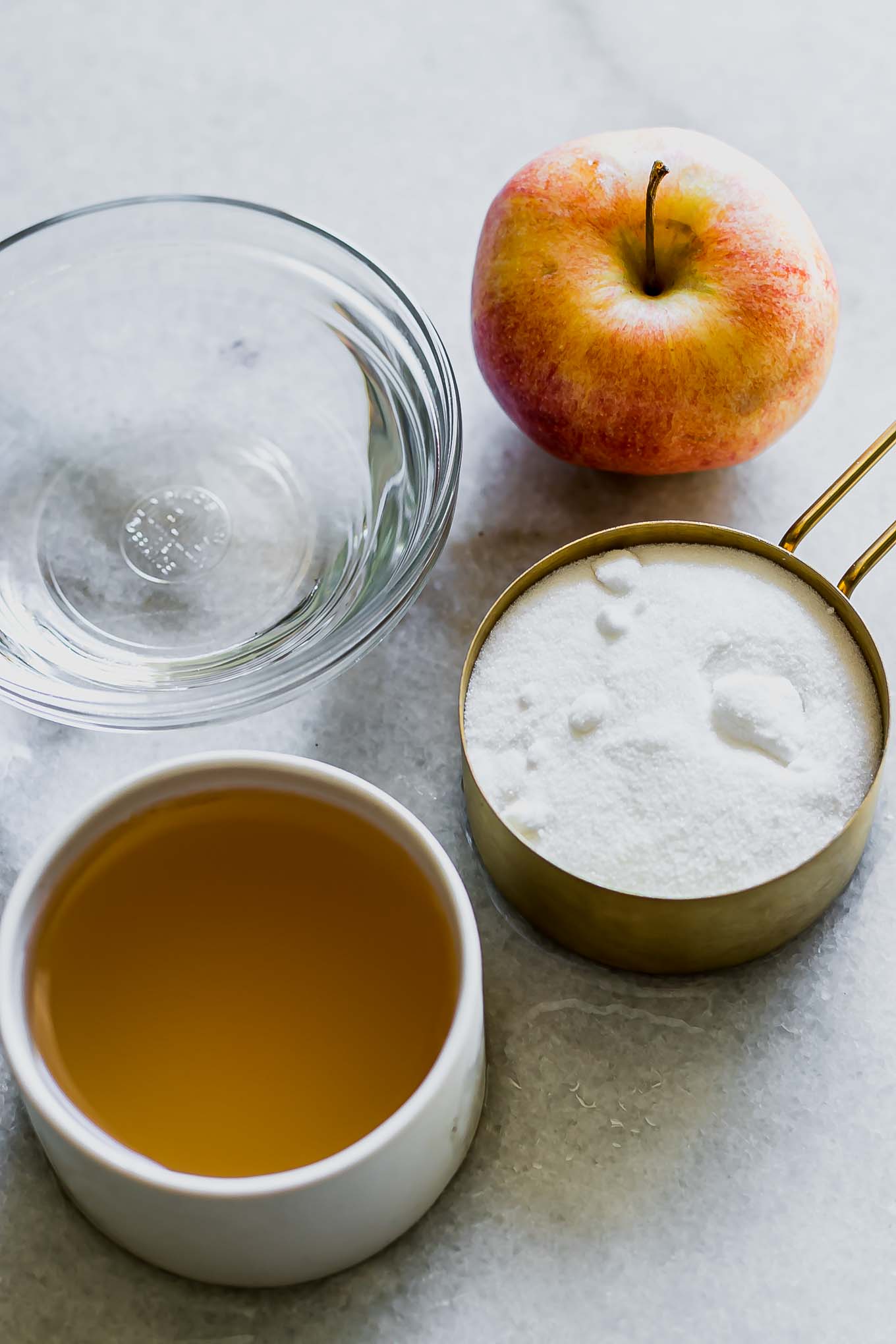 bowls of sugar, apple juice, water, and an apple for simple syrup on a white marble table