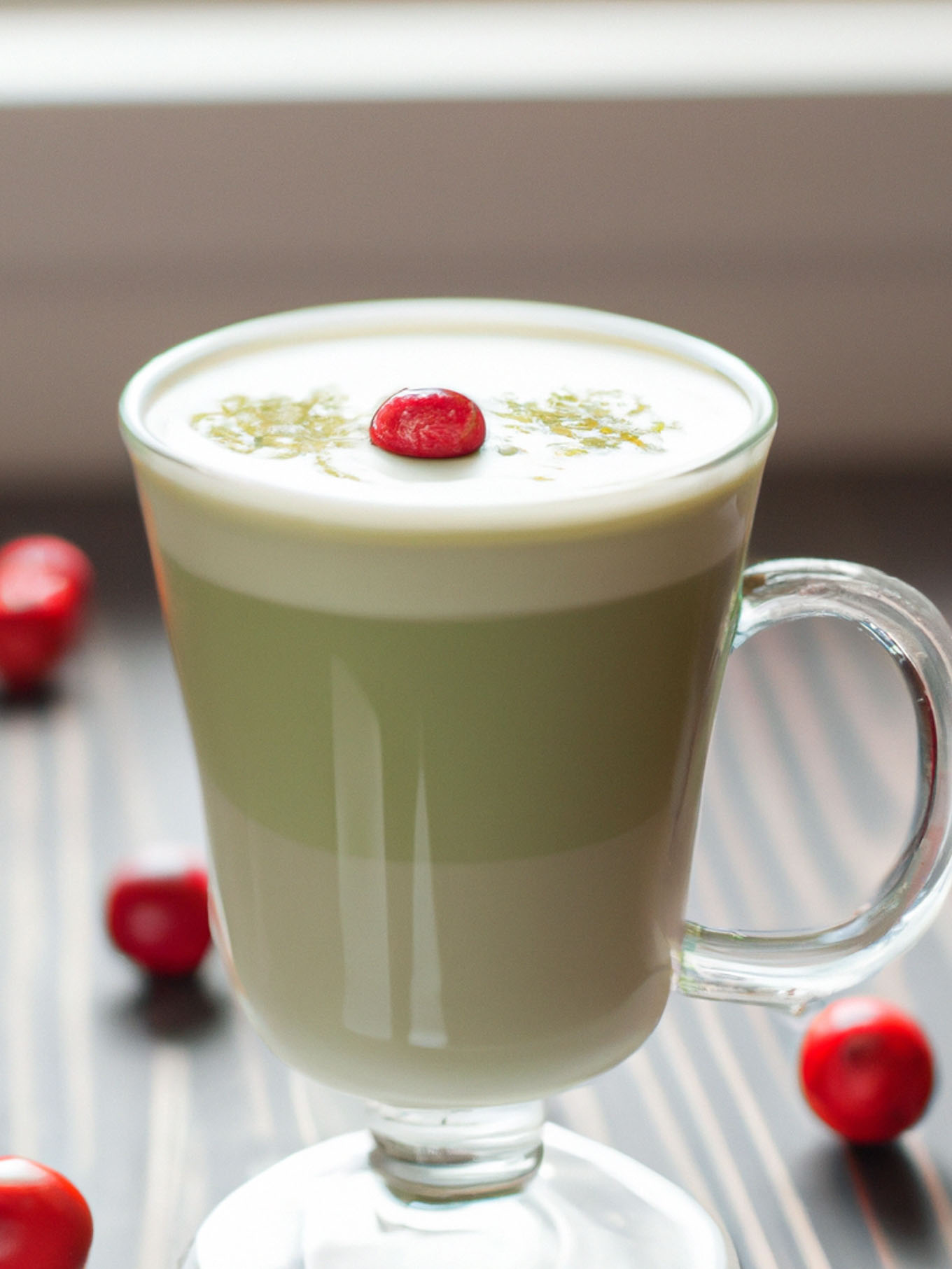 a hot matcha latte in a glass with a cranberry garnish